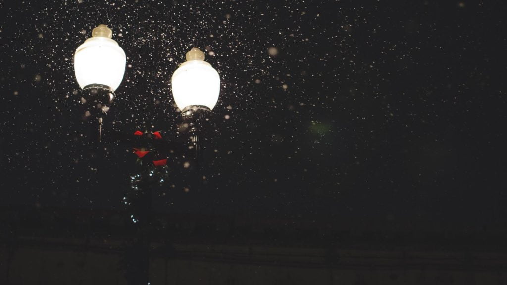 A night time photo of stylized street lights highlighting falling snow