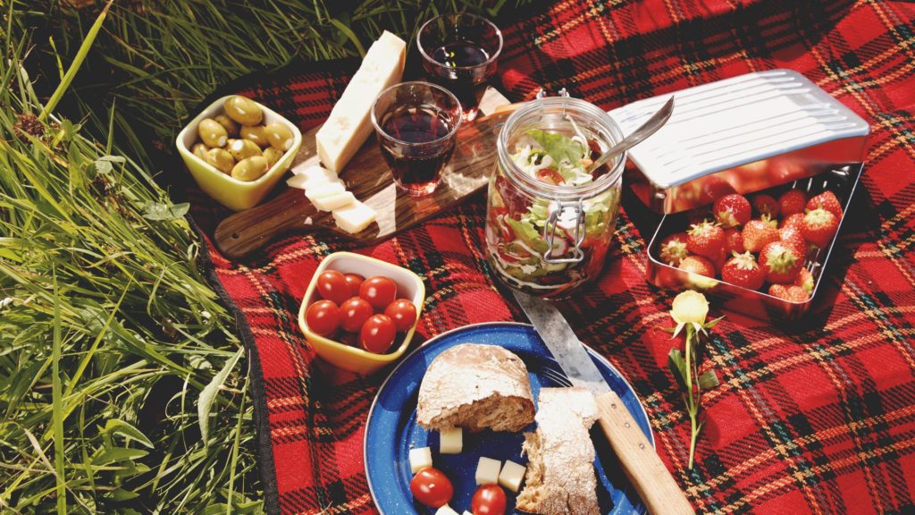 Plaid blanket laid on the grass with an assortment of food and snacks laid upon it