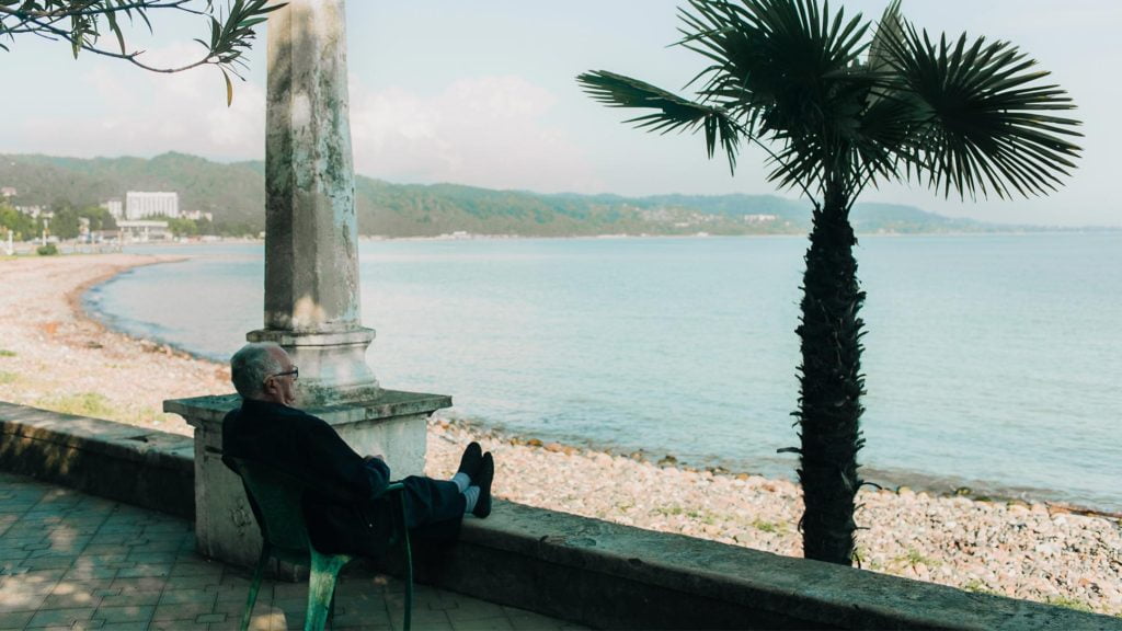 Photo of older male sitting in a chair relaxed while looking out at the beach