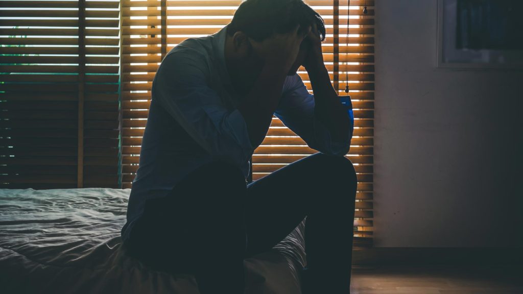Man sitting on his bed after work with hands on his head feeling stressed