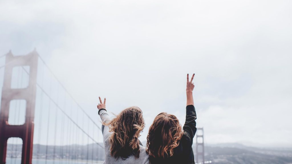 Two females facing the Golden Gate Bridge holding up peace signs