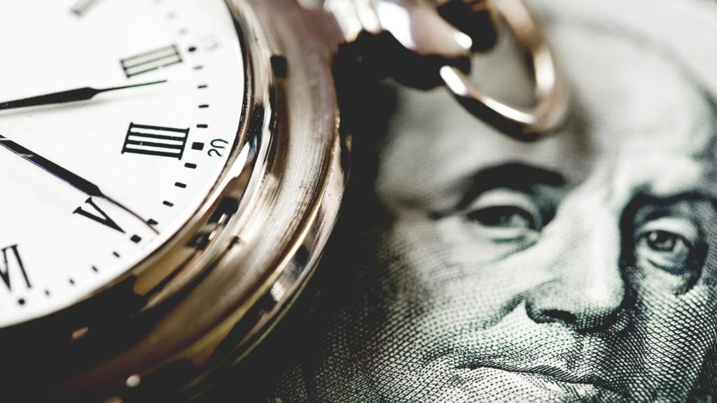 Pocket watch laying on top of a dollar bill in US currency